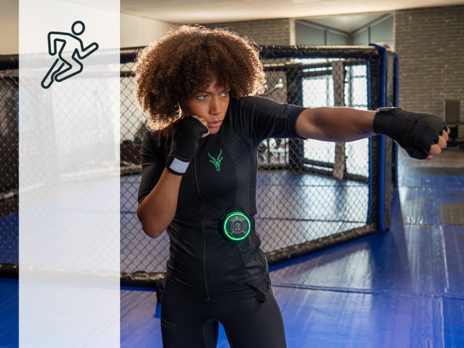 Młoda kobieta wykonuje ćwiczenia kickboxingu w mobilnym kombinezonie EMS Antelope. Ma brązowe loki i patrzy w prawo ze skupieniem, wyciągając lewą pięść do przodu i chroniąc twarz prawą pięścią. W tle widać studio bokserskie.