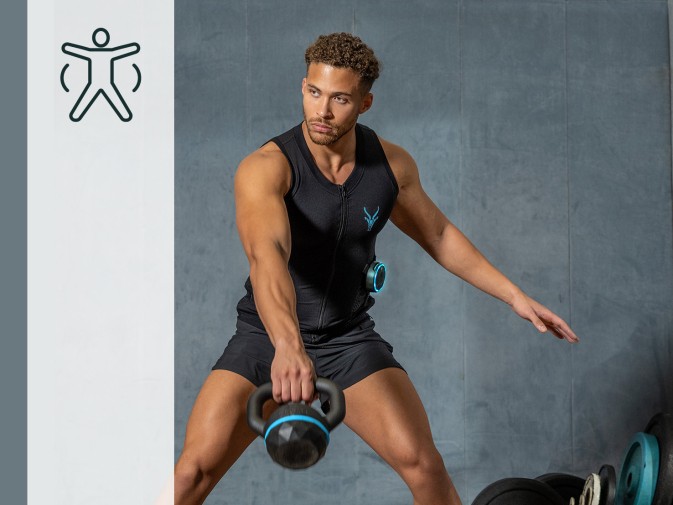 Młody mężczyzna trenuje z kettlebells na siłowni. Ma na sobie kombinezon Antelope EMS.