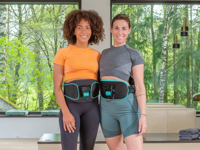 Zwei Frauen stehen nebeneinander und tragen den Corefit EMS-Gürtel.