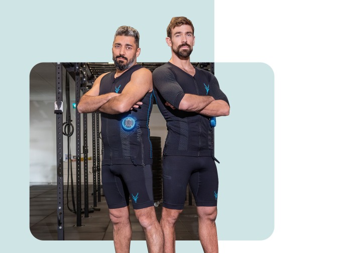 Deux hommes se tiennent dos à dos dans un gymnase. L'homme de gauche porte un débardeur EMS d'Antelope, l'homme de droite une combinaison EMS.