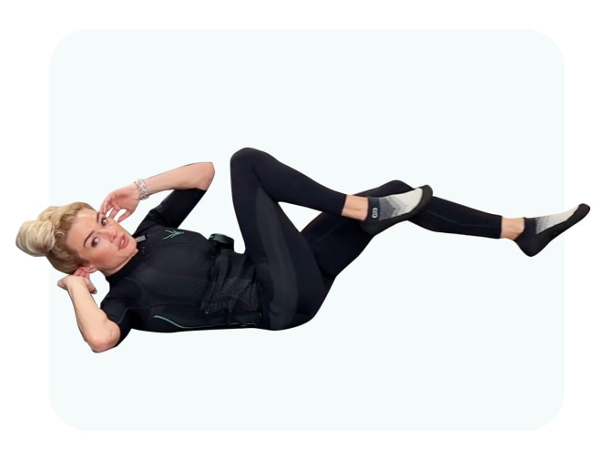 Jessica führt einen Bicycle Crunch auf dem Boden aus. Sie trägt den EMS Anzug von Antelope.