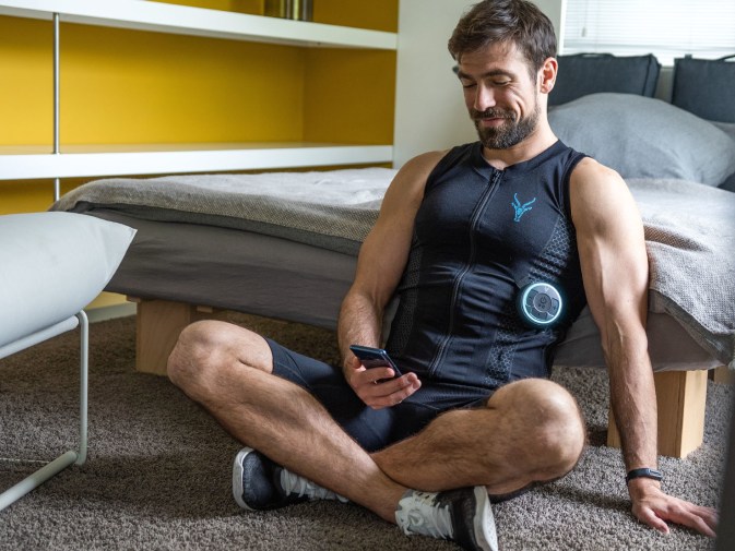 A man is recovering after his workout while wearing the EMS tank top. He is sitting on the floor and setting up the Antelope Go app.
