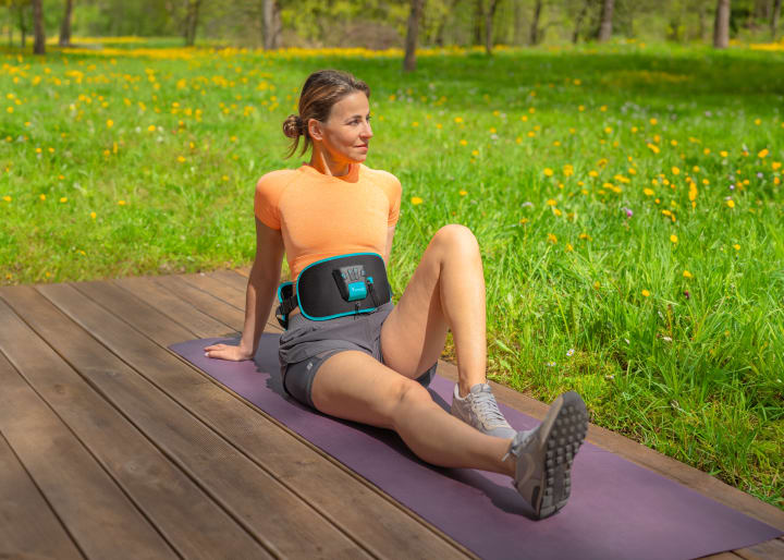 A woman outside on a mat relaxing after EMS core training with Corefit II.