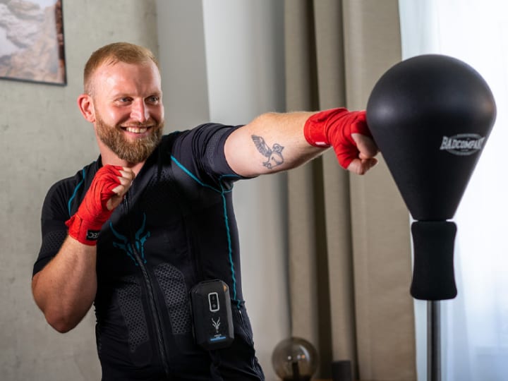 Christoph Rüsseler wearing an EMS suit performs a kickboxing exercise. He is smiling.