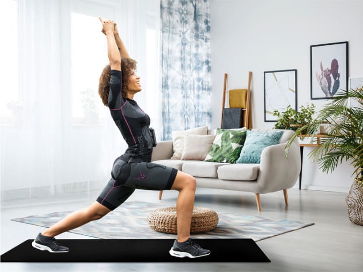 A woman wears an EMS suit while performing a yoga pose on a mat at home.
