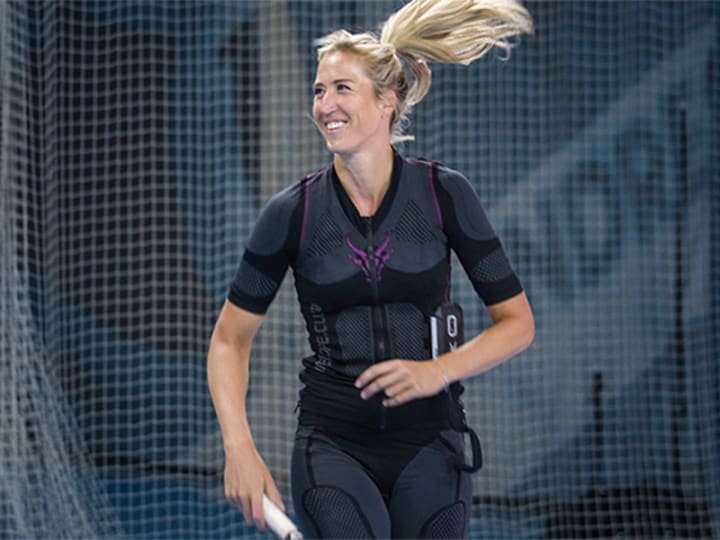 Sophia Bergner plays tennis in an EMS suit on a tennis court. She smiles.