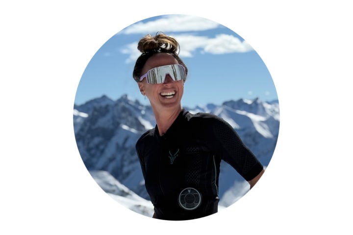 Ein Portrait von Marina. Sie trägt den Antelope EMS-Anzug und lächelt in die Kamera. Hinter ihr sind verschneite Berge.