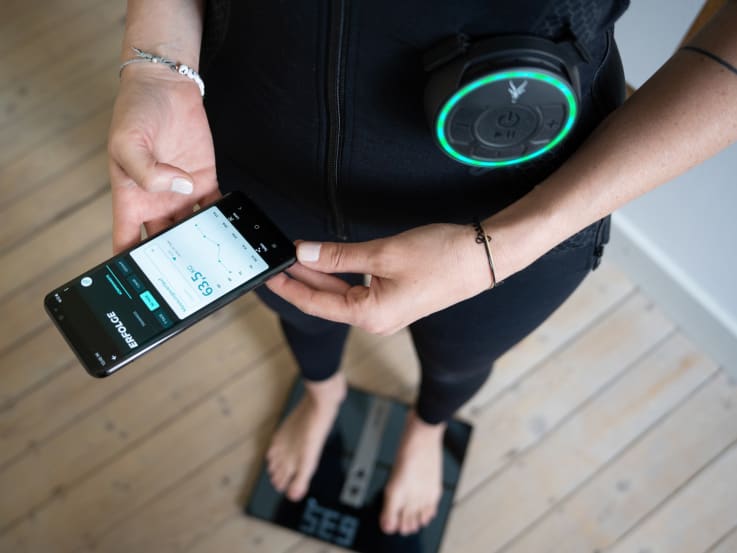 A woman stands on a Beurer smart scale and tracks her weight loss in the Antelope Go app.