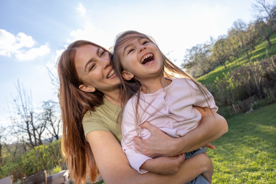 Lachende Frau umarmt lachendes Kind im Garten