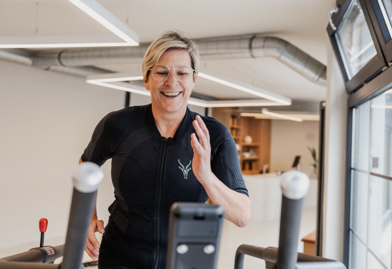 Eine Frau im EMS-Anzug von Antelope läuft auf einem Laufband im Fitnessstudio. Sie lächelt dabei.