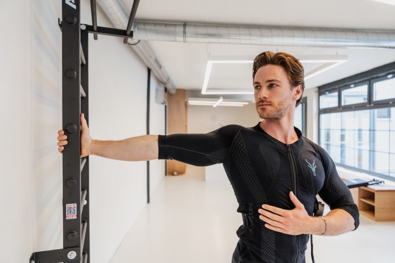 Ein Mann im EMS-Anzug von Antelope dehnt seine Brust in einem Fitnessstudio.