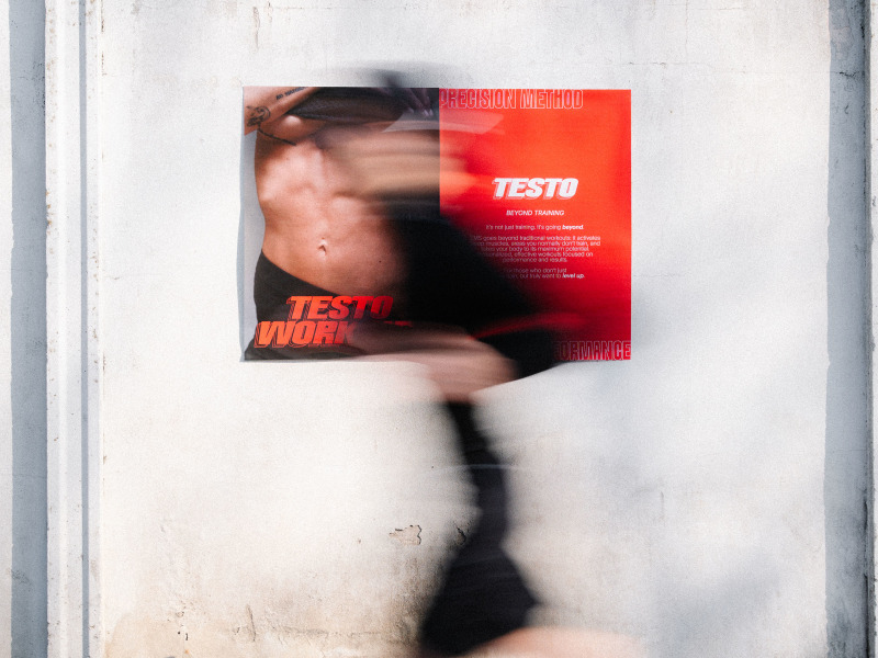 Eine Person bewegt sich unscharf an einer Wand vorbei, vor der ein rotes Poster von TestoWorkout angebracht ist.