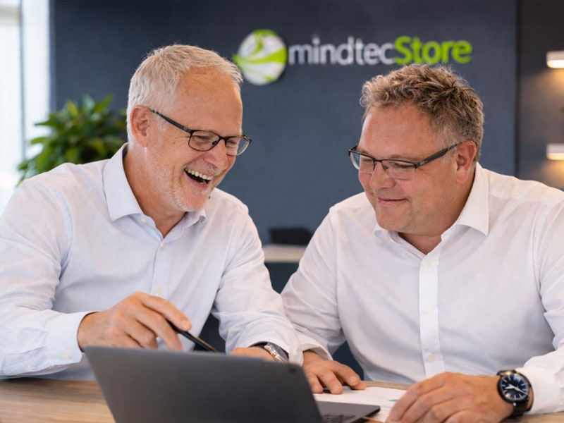 Die Geschäftsführer von MindTecStore, Harald Baums (links) und Hans‑Georg Bieschke (rechts), arbeiten gemeinsam an einem Laptop.