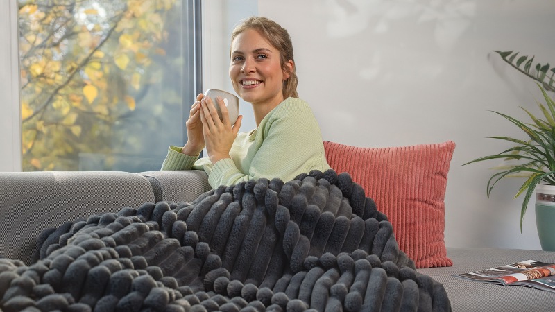 Frau sitzt eingekuschelt auf dem Sofa unter einer Decke und hält ein Taschentuch in den Händen.