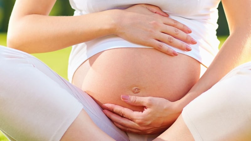 Schwangere Frau hält mit beiden Händen sanft ihren Bauch