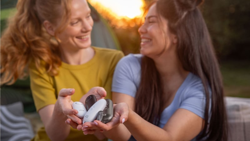 Two young women are out in the countryside, holding several Beurer insect bite relief products in their hands and smiling at each other
