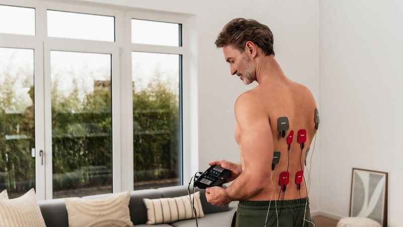 Mann benutzt EM 59 TENS Gerät von Beurer im Wohnzimmer