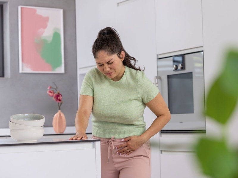 Frau steht in der Küche und hat Menstruationsschmerzen