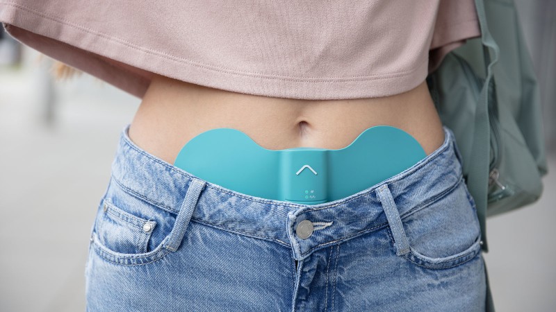 Frau trägt das Beurer EM 55 Menstruations-Pad am Unterbauch gegen Regelschmerzen, unterwegs im Freien.