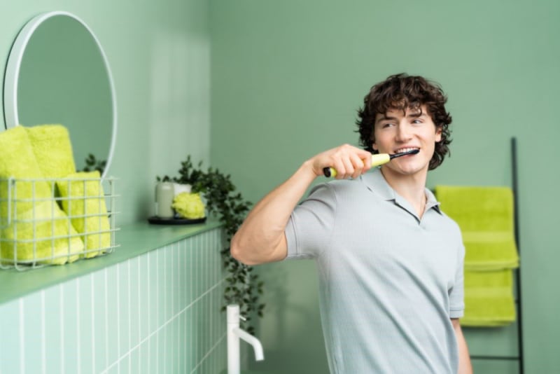 A young man brushes his teeth in the bathroom with the Beurer SC 50 electric toothbrush.