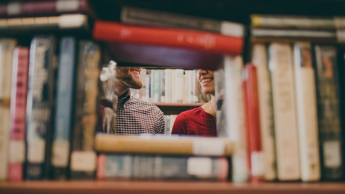 A man and a woman smiling at each other in a library.