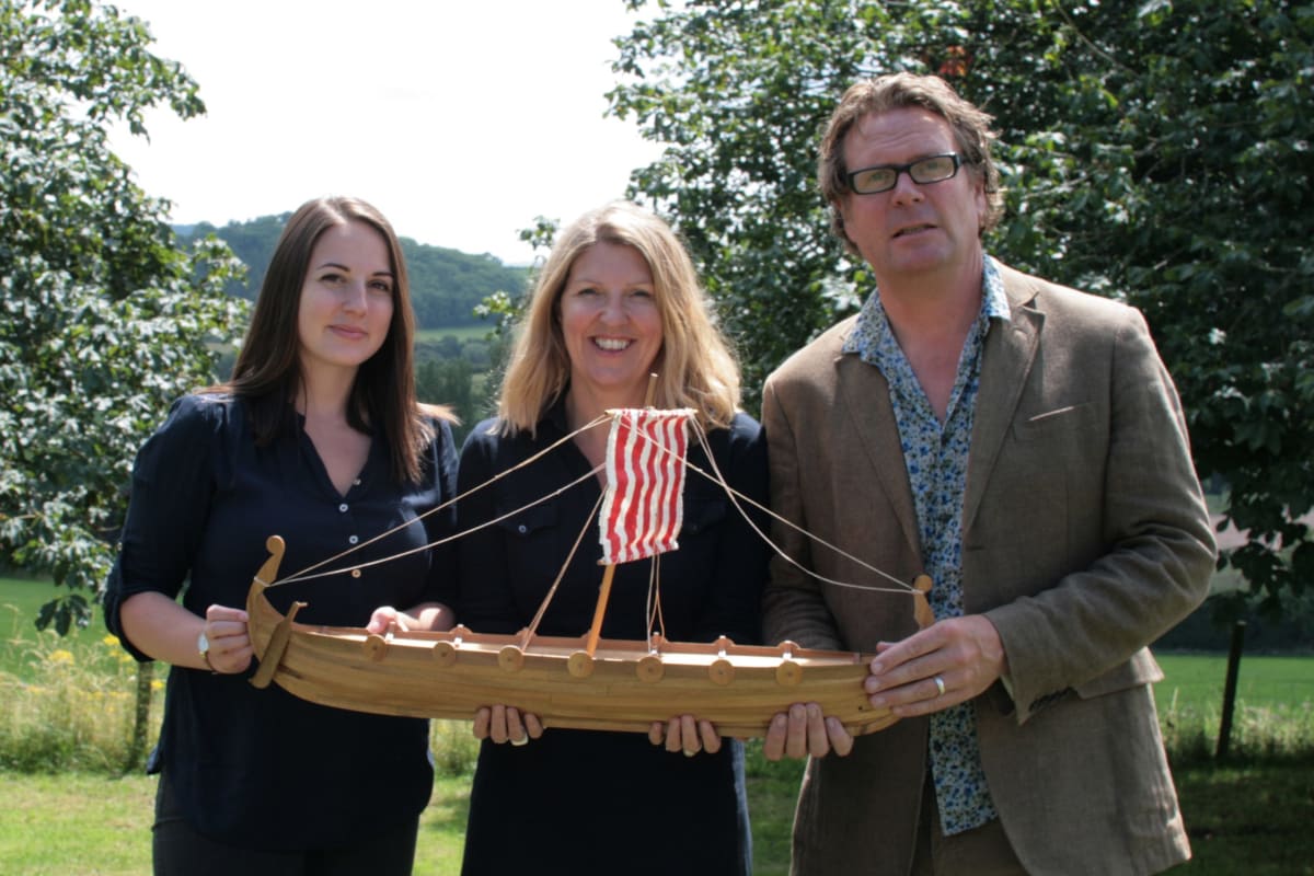 The team from Scattering Ashes hold up a mini Viking funeral boat.