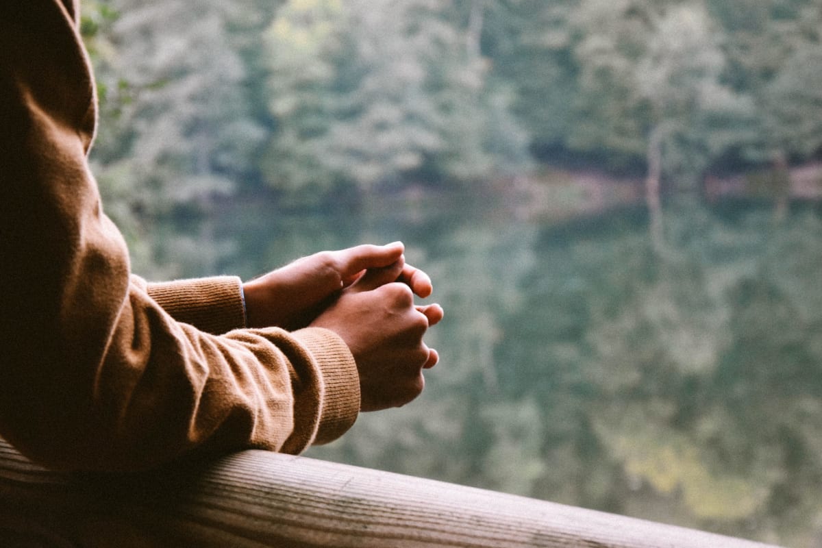 Person leaning against a fence by a lake