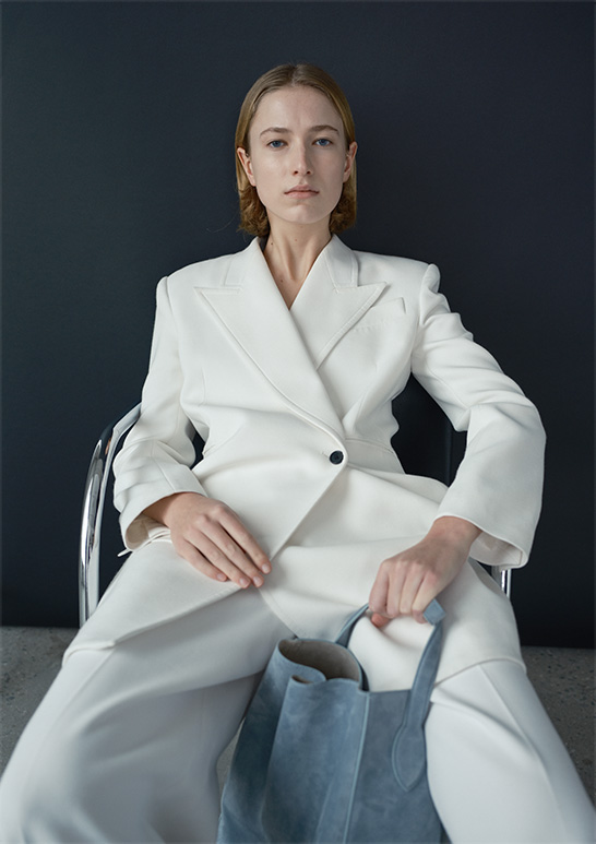 Model Wears Khaite - Jacobson One-Button Jacket, Bacall Straight Leg Pants, and Frida North-South Calfskin Tote Bag