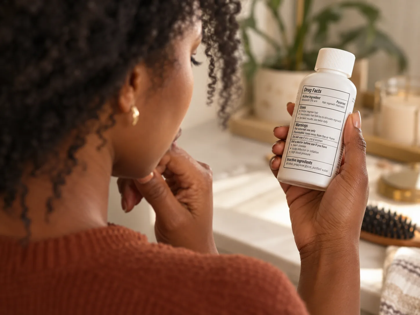 A woman reading the Drug Facts label on a minoxidil bottle, including the inactive ingredients list