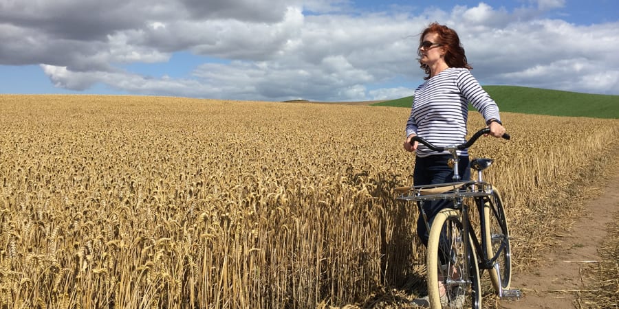 A photo of a woman on a bicycle overlooking a field.