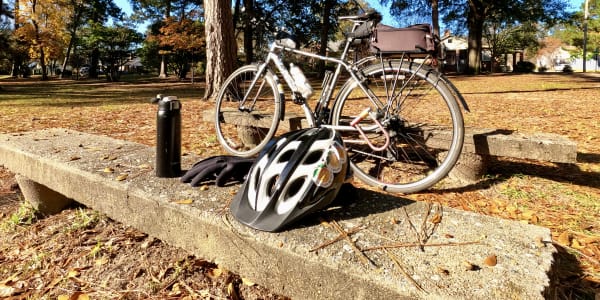 A photo of a bicycle with a helmet, gloves, and a coffee thermos.