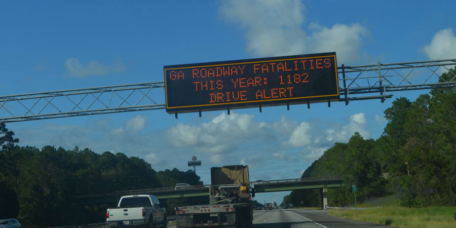 Traffic sign that reads: "GA ROADWAY FATALITIES THIS YEAR: 1182 / DRIVE ALERT."