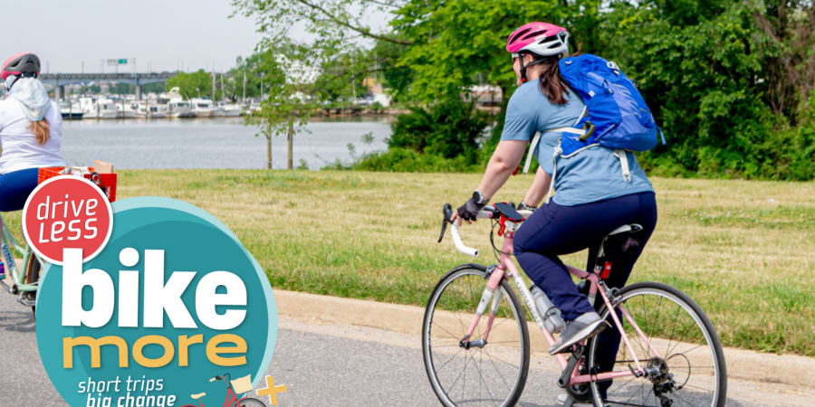 A promotional graphic for "Drive Less, Bike More" showing a woman riding a bicycle.