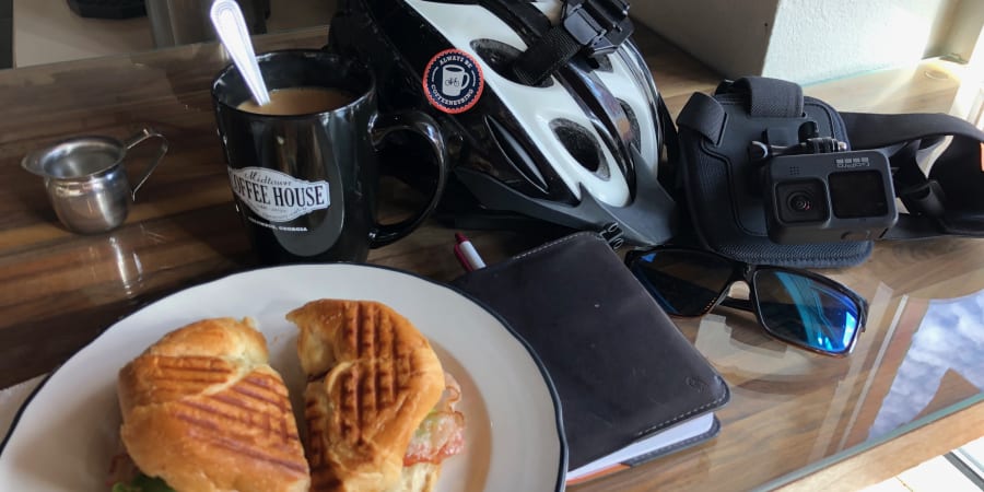 A photo of a sandwich, a mug of coffee, a bicycle helmet, and a GoPro camera on a counter.