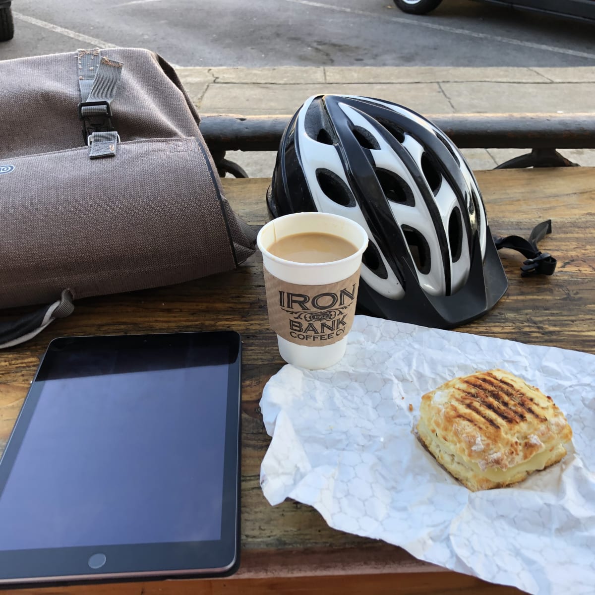 A photo of my bag, helmet, iPad, and coffee on an outdoor table.