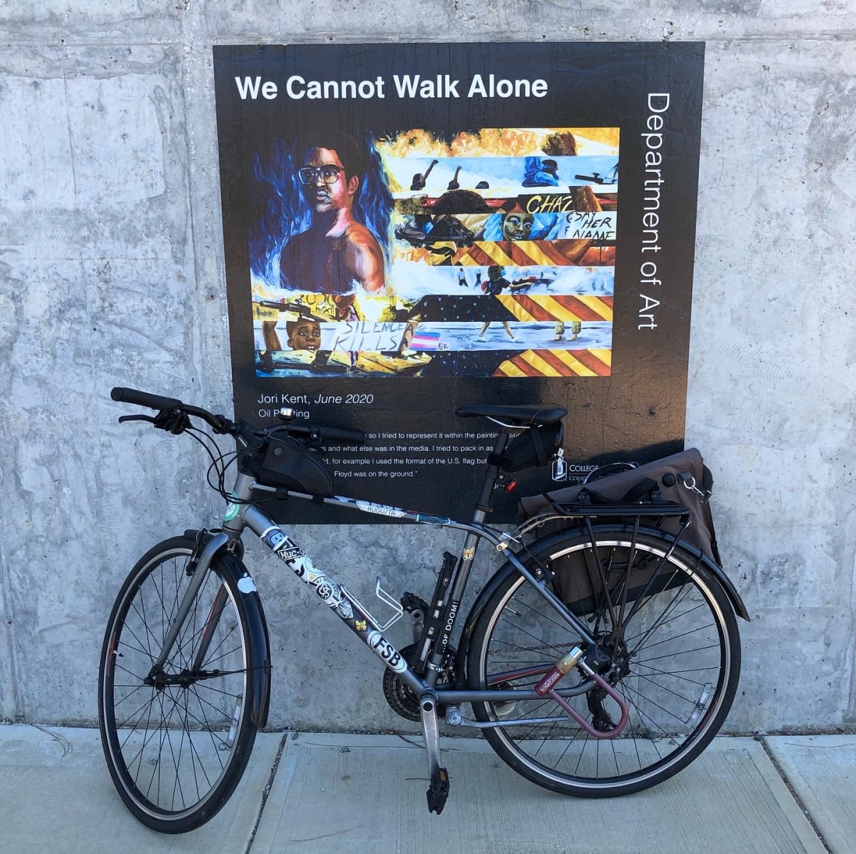 A photo of my bicycle in front of an art piece titled "We Cannot Walk Alone."