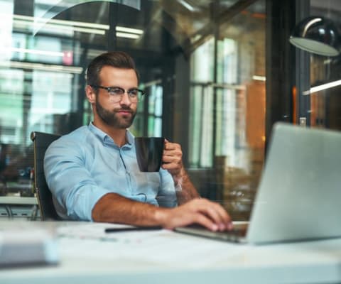 Man working on laptop holding mug