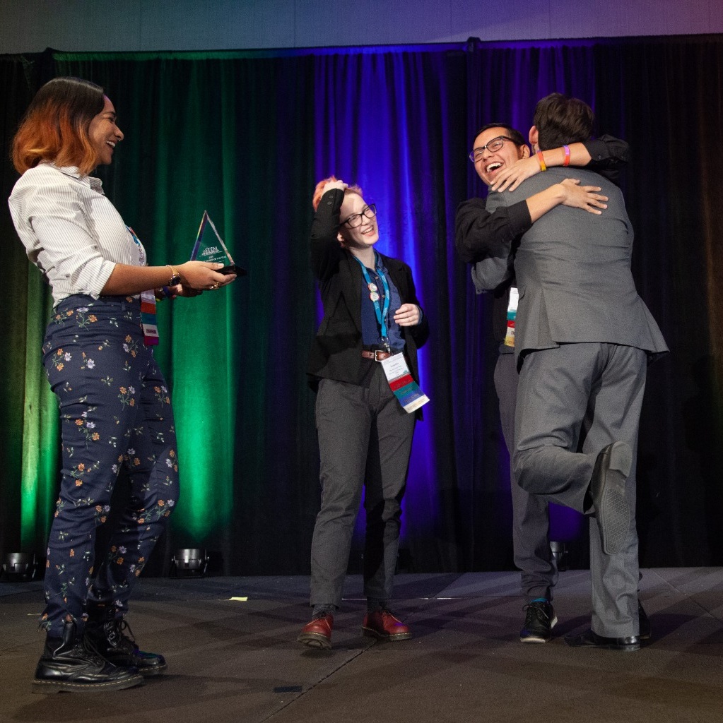An award being presented as awardees hug on stage