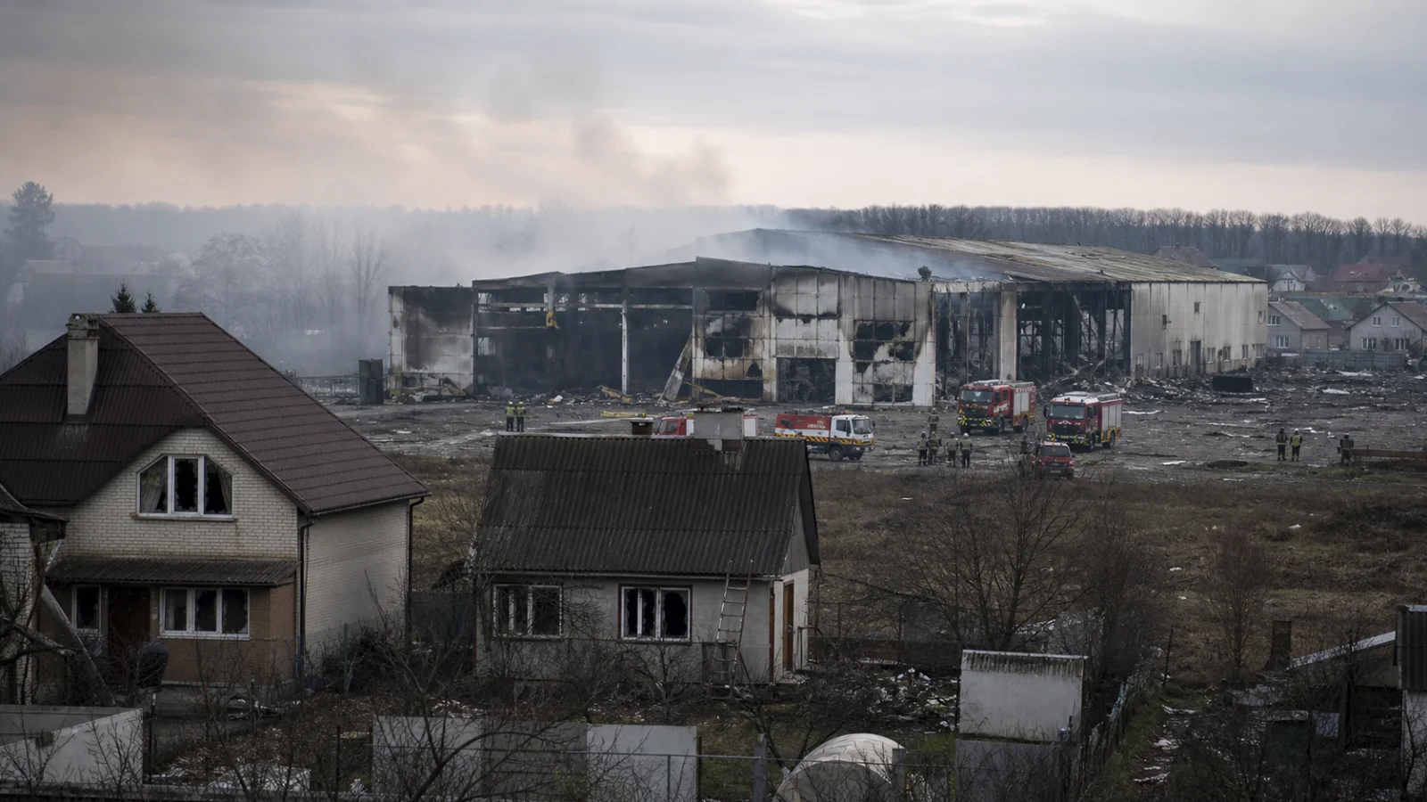 AI editorial illustration of a damaged warehouse and emergency response near homes west of Kyiv