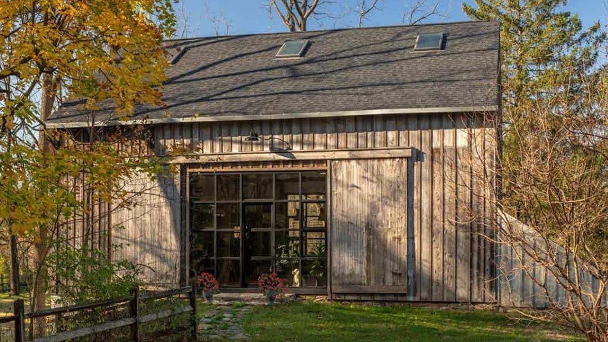 Exterior of a weathered wood barn with sliding doors, glass entry, and skylights, surrounded by autumn trees.