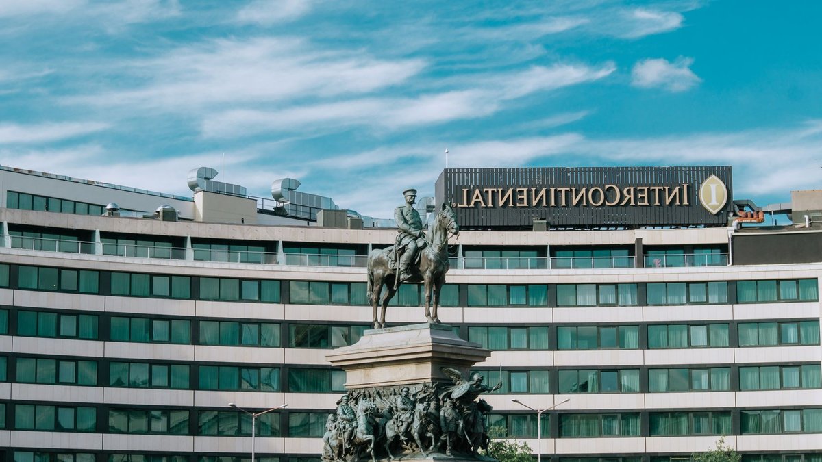2027 Hotel Playbook: Invest with Purpose Operate with Discipline Equestrian statue in urban setting with Intercontinental Hotel background.