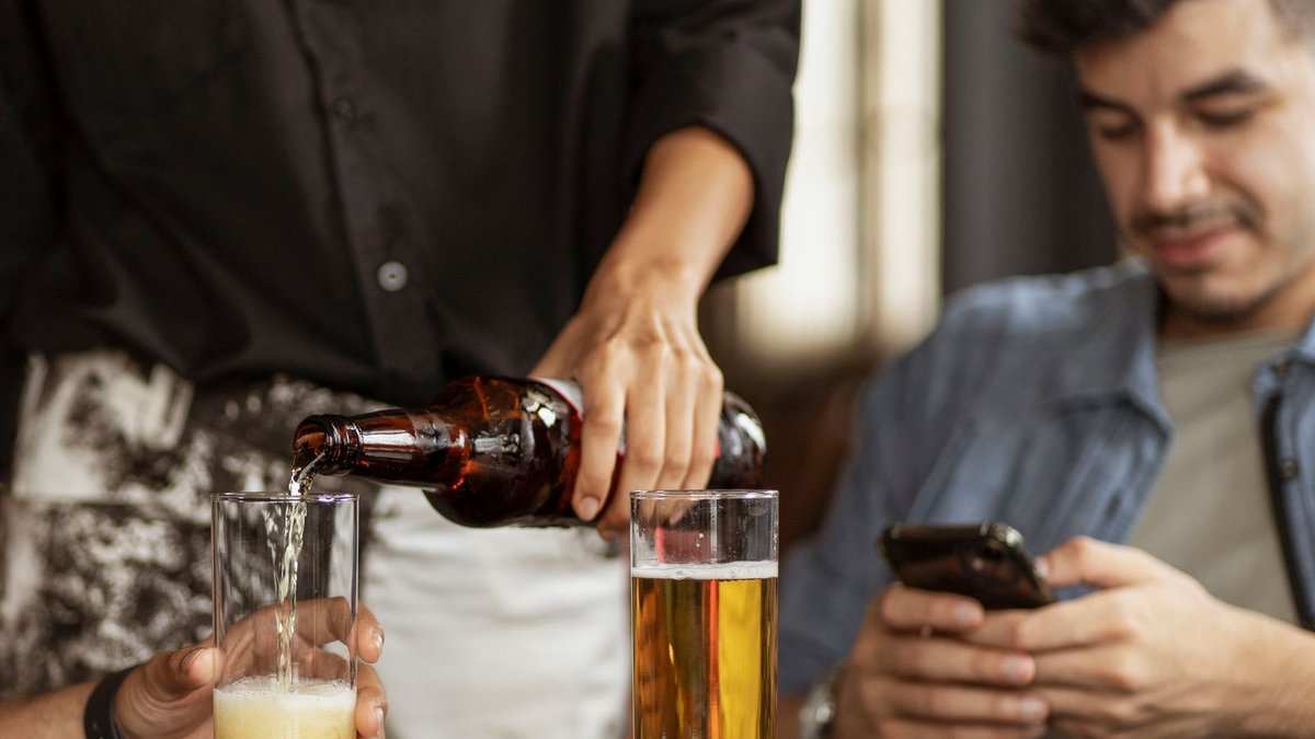 Krones highlights alcohol-free and digital trends at BrauBeviale Two people enjoying a laid-back bar setting with beer, one on a phone and a server pouring drinks.