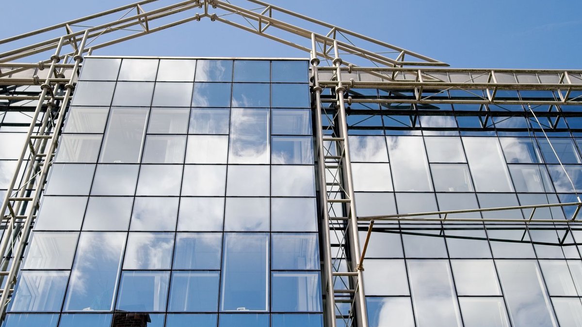 Contemporary glass facade reflecting clouds under a clear blue sky, showcasing modern architecture.
