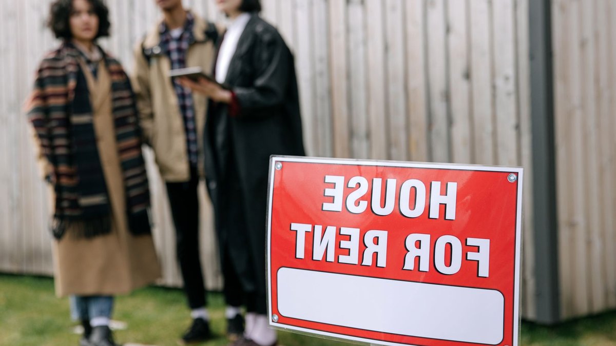 ARL Announces AI Summit for Build-to-Rent Sector in Manchester Three adults examining a house for rent sign outdoors, depicting diverse and inclusive interest in rental properties.