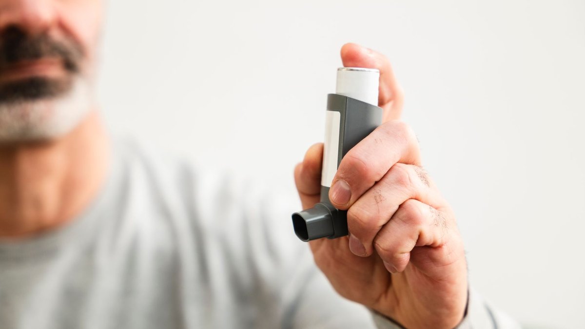 Malaysia expands respiratory care to 902 clinics Middle-aged man using an inhaler to manage respiratory issues indoors.