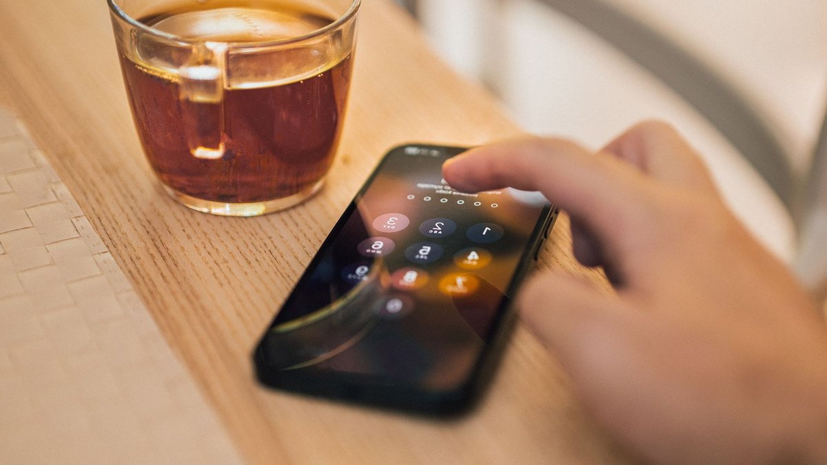 MGAs Leverage Tech, Data to Lead in Competitive Insurance Market Close-up of hand unlocking a smartphone next to a cup of tea on a wooden table, emphasizing technology and security.