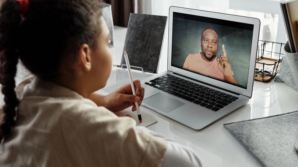 US schools to limit screen time in classrooms A child engaged in online learning with a teacher on a laptop during a virtual session indoors.
