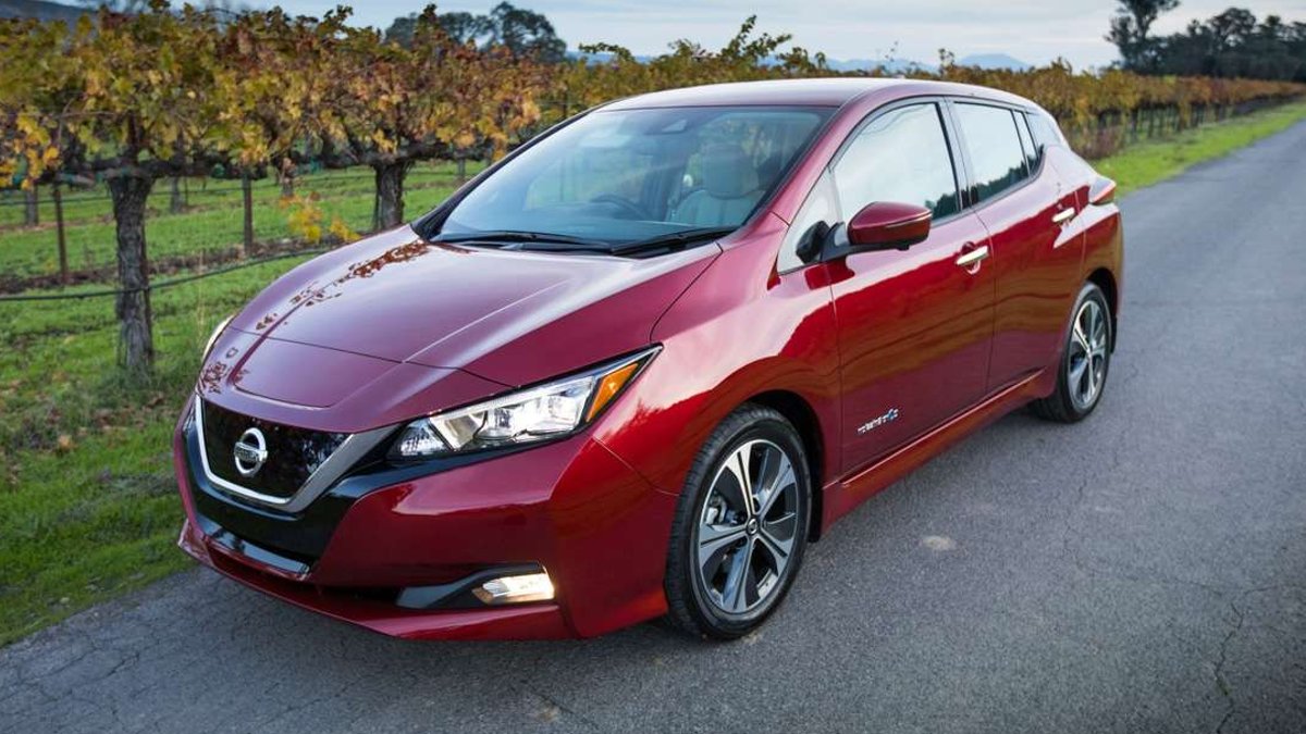Red 2018 Nissan Leaf electric hatchback shown from a front three-quarter angle on a rural road beside a vineyard.