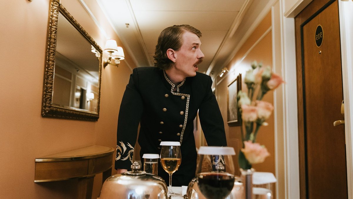 Hotel porter in vintage uniform delivering room service in a luxurious hallway.