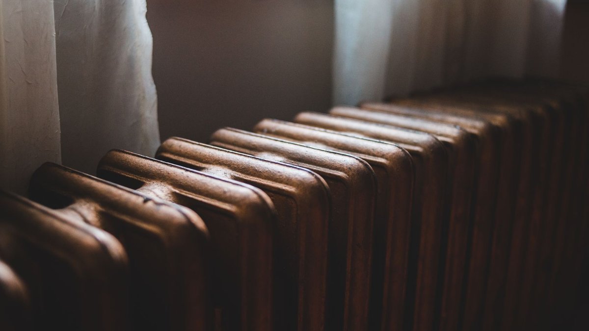 Retrofitting Underfloor Heating Costs £36-£120 per m² Aged heating battery made of cast iron near windowsill with curtains in house.